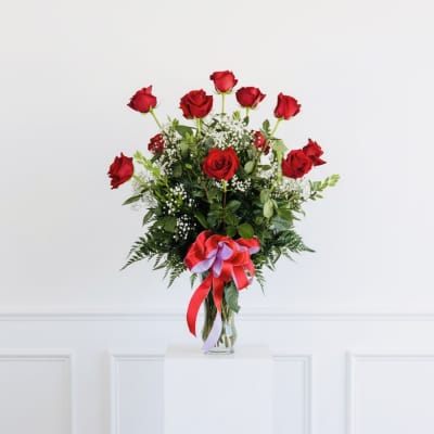 Red roses arranged in a clear glass vase with a ribbon bow