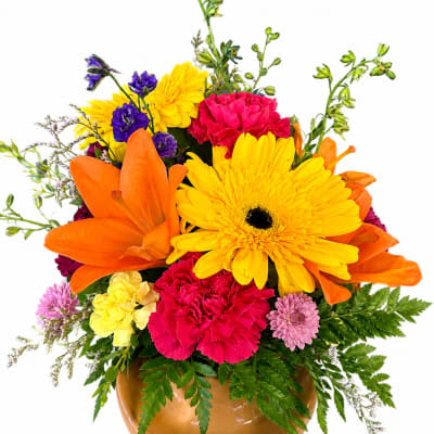 Bright mixed bouquet in a brown vase with yellow, orange, pink, and purple flowers.