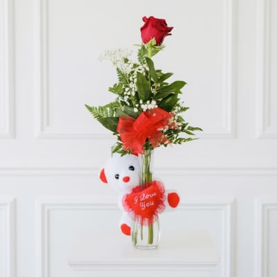 Single red rose in a glass vase with a teddy bear and heart decoration