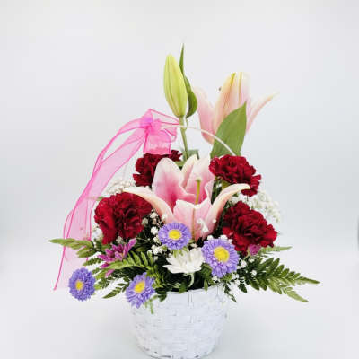Pink lilies and red carnations in a white basket with a pink ribbon