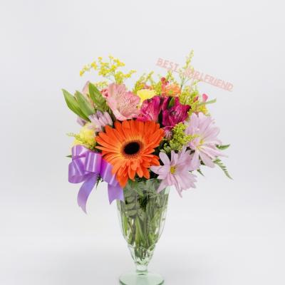 Colorful mixed bouquet in a clear glass vase with a purple ribbon