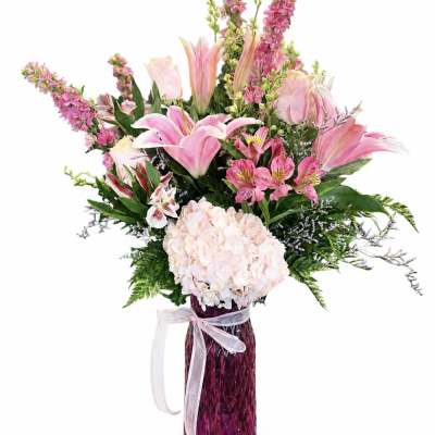 Pink lilies and hydrangea in a tall purple vase with a ribbon