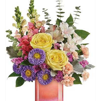 Bouquet of yellow roses, purple daisies, and pink flowers in a pink glass vase