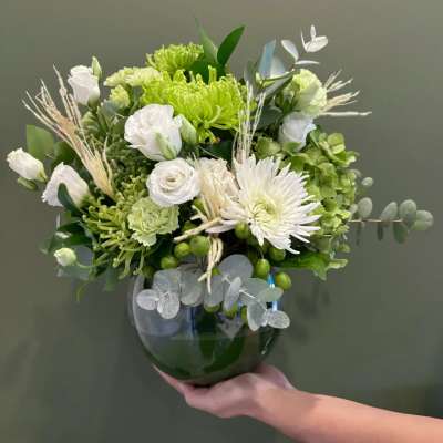Green and white floral arrangement in a dark glass vase