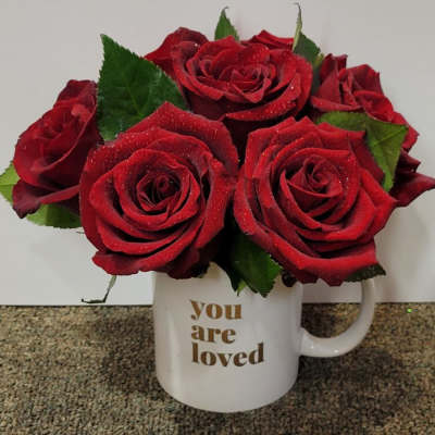 Red roses arranged in a white mug with "you are loved" text