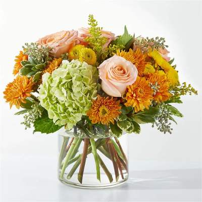 Bouquet of peach roses, green hydrangea, and orange mums in a glass vase