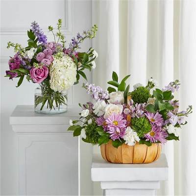 Two floral arrangements with pink, white, and purple blooms in a glass vase and a pumpkin container.