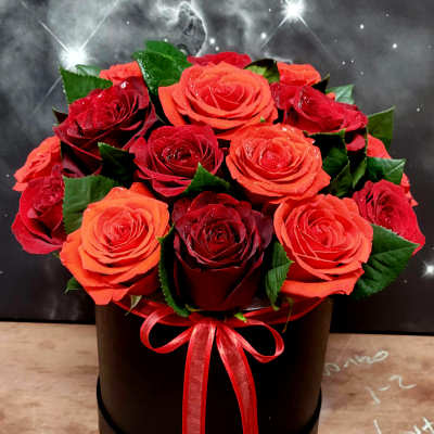 Red and orange roses arranged in a black round box with a red ribbon