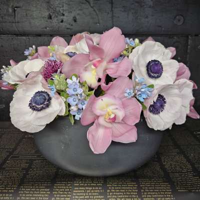 Pink orchids and white anemones arranged in a dark bowl
