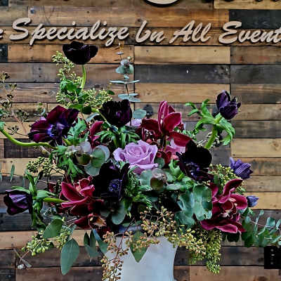 Purple and burgundy floral arrangement in a white pedestal vase