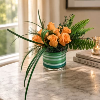Orange roses in a striped glass vase with long green foliage