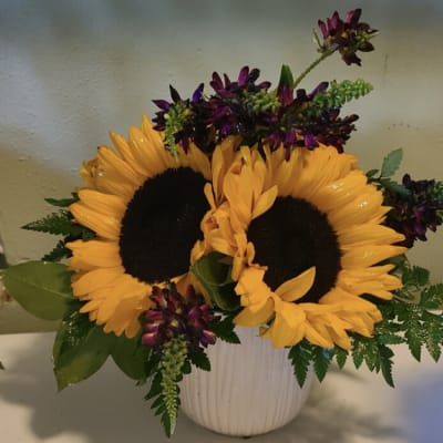 Sunflowers and purple flowers arranged in a white vase