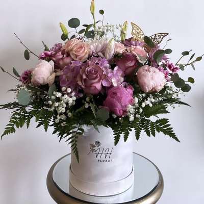 Pink and lavender roses arranged in a white hat box with greenery.