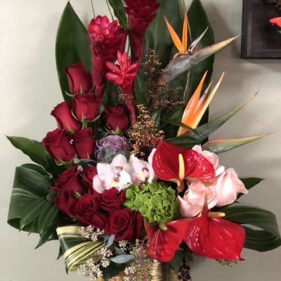 Tall tropical bouquet with red roses, anthuriums, and orchids in a gold vase