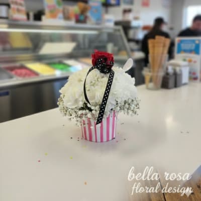 White floral arrangement in a pink striped container with a red rose topper