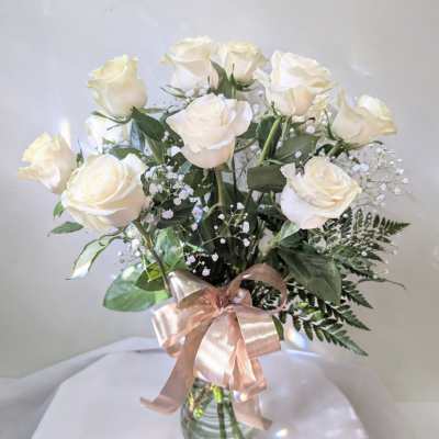 White roses in a glass vase with a pink ribbon