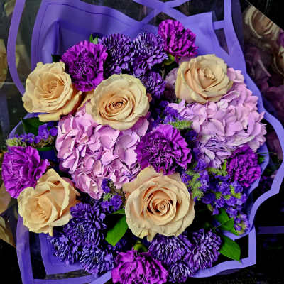 Bouquet of peach roses, purple chrysanthemums, and pink hydrangeas wrapped in purple paper