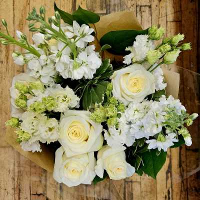 Bouquet of white roses and white stock flowers wrapped in brown paper