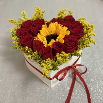 Heart-shaped box of red roses with a sunflower center and red ribbon