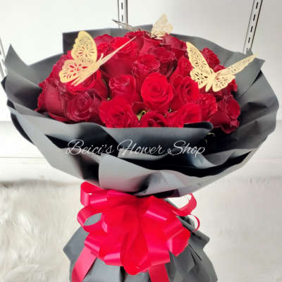 Bouquet of red roses wrapped in black paper with a pink ribbon