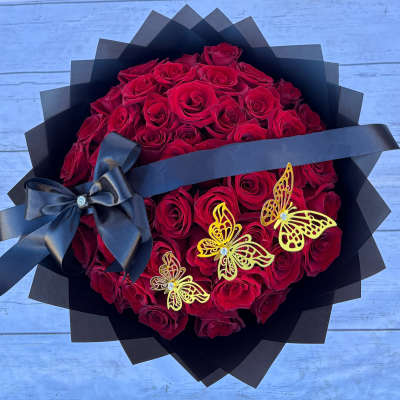 Bouquet of red roses wrapped in black paper with a black ribbon and butterfly accents