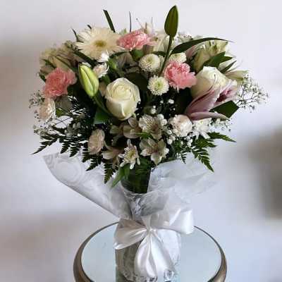 Bouquet of white and pink flowers in a clear glass vase with a white ribbon