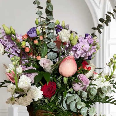 Mixed bouquet of roses, lisianthus, and purple blooms in a wicker basket