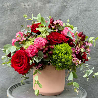 Red and pink roses arranged in a blush vase with green filler and berries.