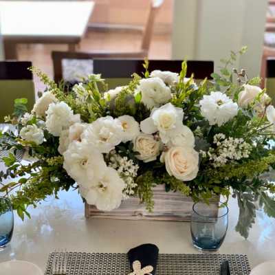 White floral centerpiece in a wooden box with blue glass cups nearby