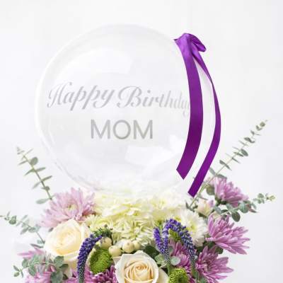 Flower box with roses and purple blooms topped by a clear balloon reading Happy Birthday Mom