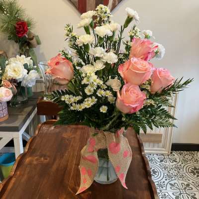 Pink roses and white carnations in a glass vase with a burlap bow