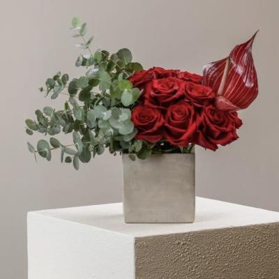 Red roses in a square vase with eucalyptus and a red anthurium
