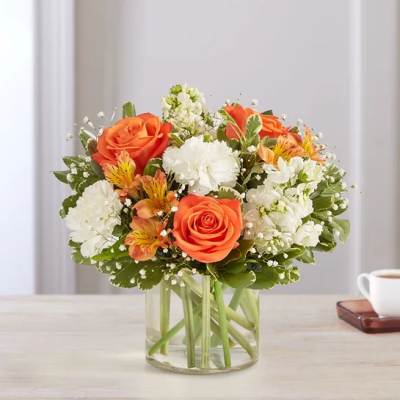 Orange roses and white flowers arranged in a clear glass vase