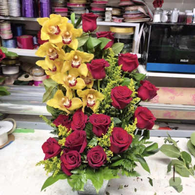 Yellow orchids and red roses arranged in a square container