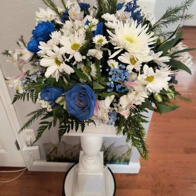 Blue and white mixed flower arrangement in a white pedestal vase
