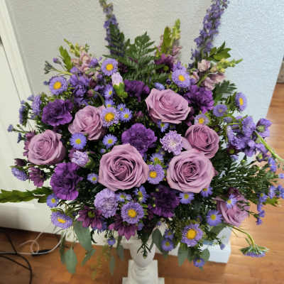Lavender roses and purple mixed flowers arranged in a white pedestal vase