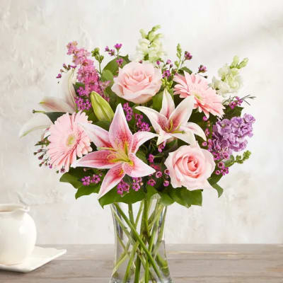 Pink roses, lilies, and gerbera daisies in a clear glass vase