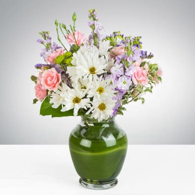Mixed bouquet of white daisies, pink carnations, and lavender flowers in a green glass vase