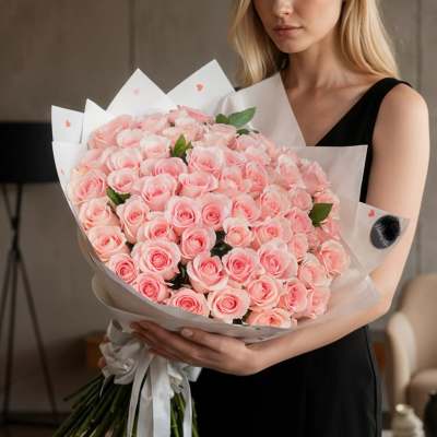 Woman holding a large bouquet of pale pink roses wrapped in white paper