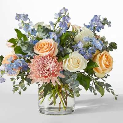 Mixed bouquet of roses, chrysanthemums, and blue flowers in a glass vase