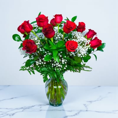 Red roses arranged in a clear glass vase with white filler flowers