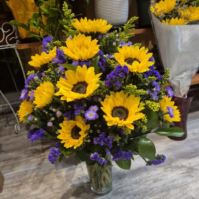 Bouquet of yellow sunflowers and purple filler flowers in a clear glass vase.