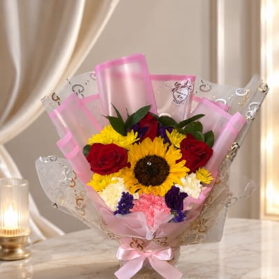 Bouquet of sunflowers, red roses, and mixed blooms wrapped in pink paper
