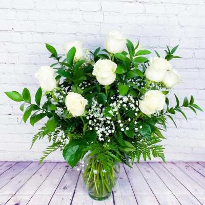White roses in a glass vase with baby's breath and greenery
