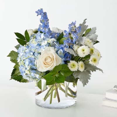 Blue hydrangeas, white rose, and white daisies in a clear glass vase