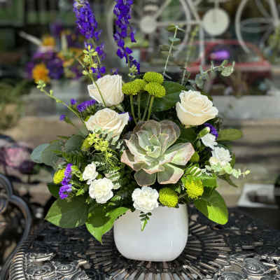 White roses and purple spikes in a white vase with a succulent centerpiece