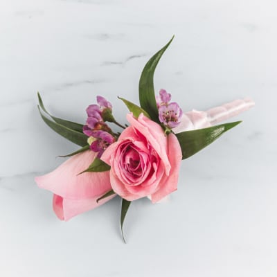 Pink rose boutonniere with small purple accent flowers wrapped in white ribbon