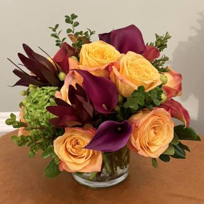 Bouquet of yellow roses and purple calla lilies in a clear glass vase