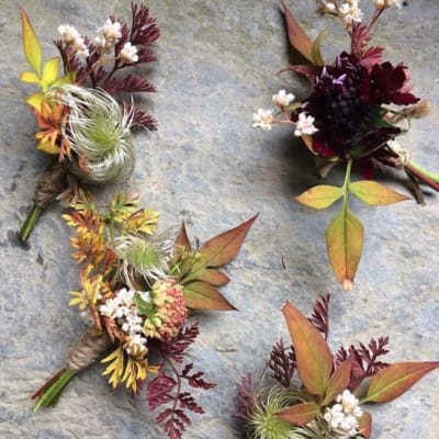 Four small floral boutonnieres with autumn-colored leaves and white accents
