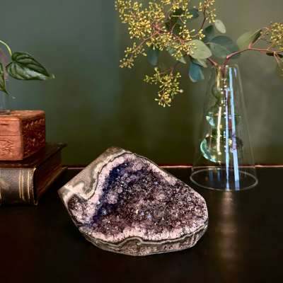 Amethyst crystal cluster on a dark surface beside a glass vase with branches
